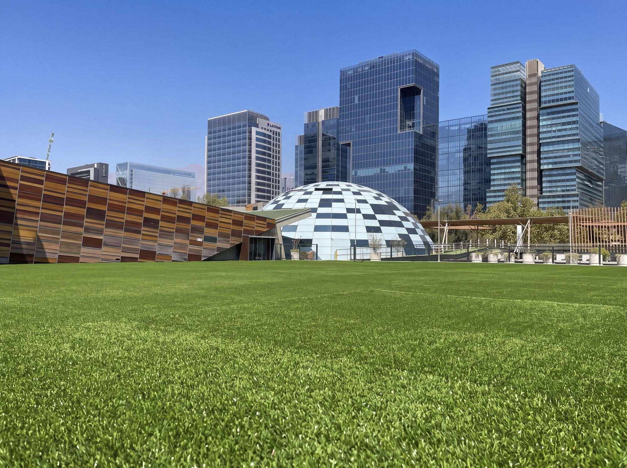 Pasto sintético instalado en Parque Araucano, con la cúpula y las torres de Las Condes de fondo